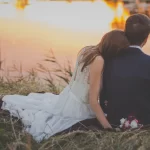 Bride and groom sitting by a lake at sunset. Can You Get Invited to a Wedding?